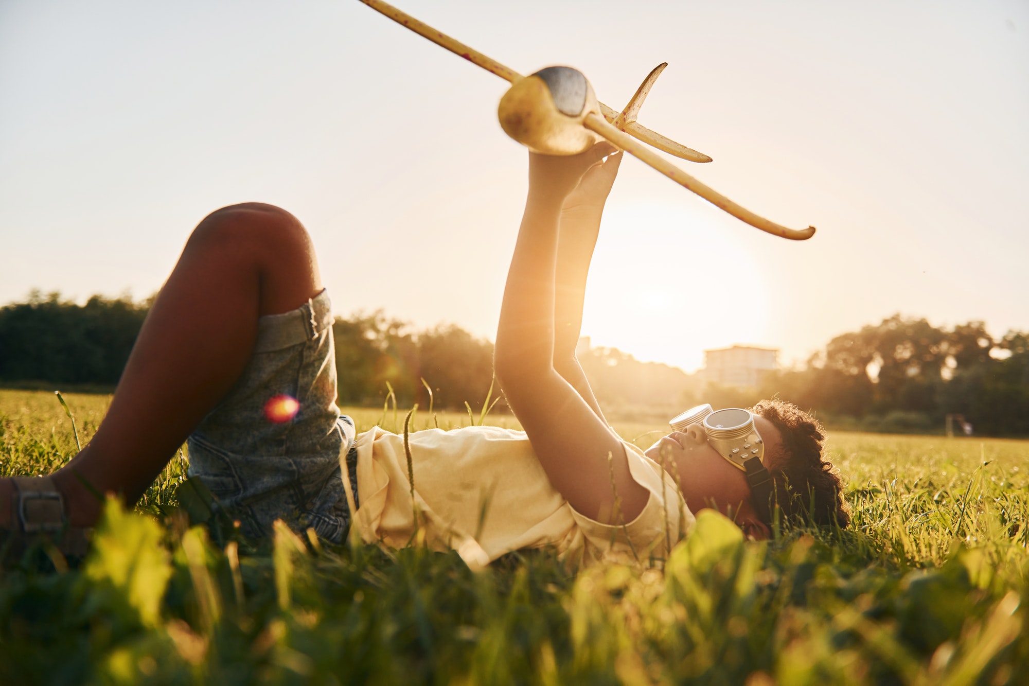 In glasses with toy plane. African american kid have fun in the field at summer daytime